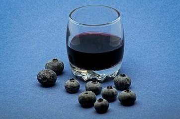 Glass of red wine with blueberries on blue background