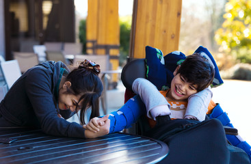 Disabled boy in wheelchair arm wrestling with caregiver outdoors