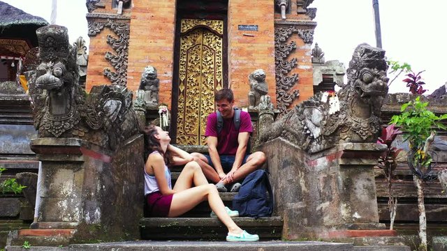 Smiling cute couple having conversation in front of golden gate of ancient temple with stone statues, exploring Asian island 