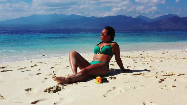Dominican Republic, young attractive woman sunbathing on the tropical sandy beach, dolly out with the sea, mountains and clouds in the background