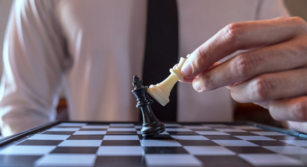 Closeup photo of businessman playing chess and beating black king