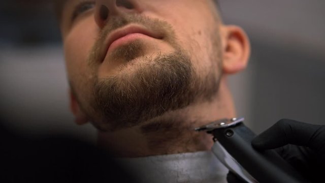 Client during beard shaving in barber shop. Hairdressing services. man cuts hair at a hairdresser-stylist in barbershop. scissors comb close-up Details of trimming. Cropped closeup  barber trimming