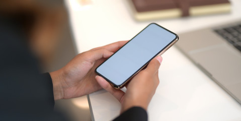 Close-up view of young businesswoman using blank screen smartphone while working on the project
