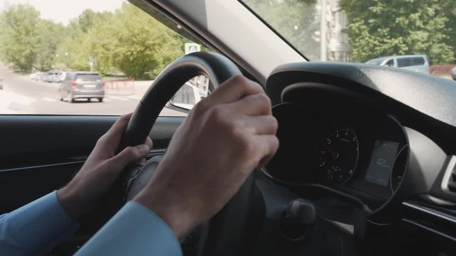 Young businessman holding steering wheel in hand while business trip in city. American entrepreneur driving car with black interior, watching front in windshield. Man wearing blue shirt is riding auto