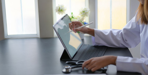 Cropped shot of young female doctor working on medical expertise with tablet in modern office