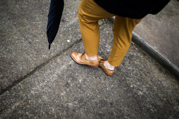 Person in gelber Hose geht schnell mit Regenschirm auf einem Asphalt Weg