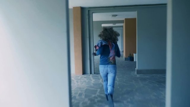 young curly haired woman running from a rapist in the lobby of building