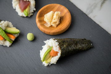 Lachs Fisch, Tunfisch und Surimi Avocado Temaki Sushi, eingelegter Ingwer und Wasabi auf Schiefer Platte und Marmor Hintergrund