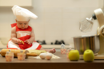 A Child, Baby, Girl, sits On The Kitchen Table, In A Cook's Cap