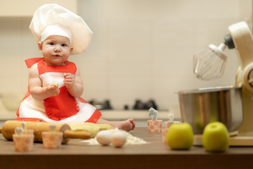 A Child, Baby, Girl, sits On The Kitchen Table, In A Cook's Cap
