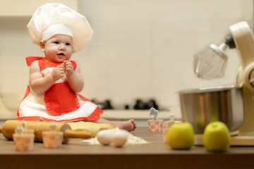 A Child, Baby, Girl, sits On The Kitchen Table, In A Cook's Cap