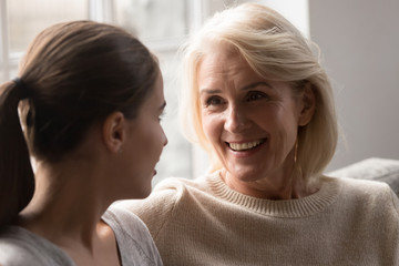 Smiling elderly mother and adult daughter chat at home