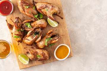 Baked quail with sauces, lime and beer on a wooden board.