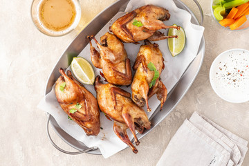 Tasty fried quail with herbs, celery, carrots and sauce on a light background.