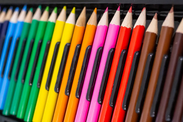 Set of bright wooden colored pencils laid out in a row with a dark background. Stationery background with an art and education Concept.