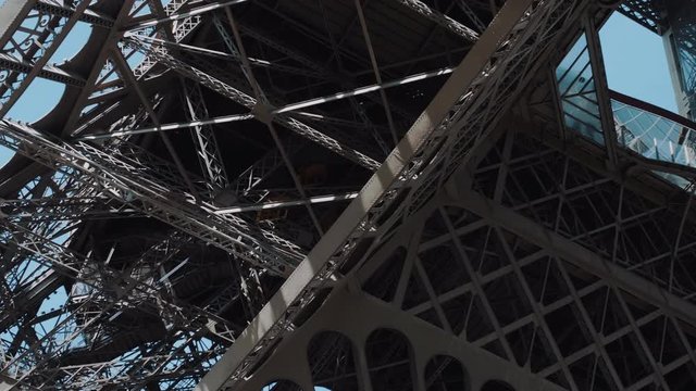 Cinematic wide shot move on funicular elevator moving upwards inside the steel structures of epic Eiffel Tower in Paris.