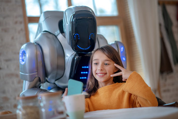 Smiling girl in orange shirt making selfie with robot
