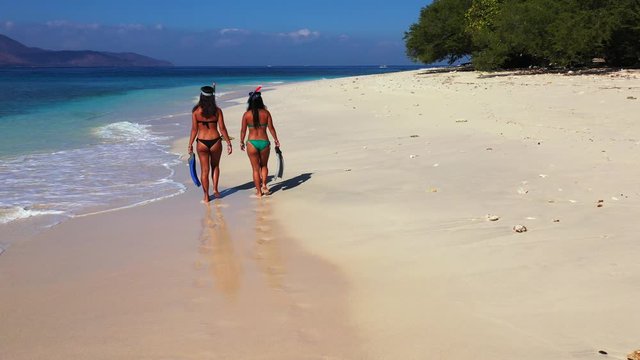 Snorkeling in the tropical ocean, two sexy ladies in the bikinis with snorkeling masks and bikinis talking on the sandy beach