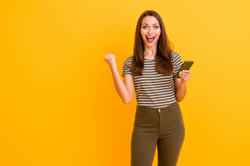 Portrait of amazed funky crazy girl use smart phone get like social media notification impressed raise fists scream wow omg wear stylish outfit isolated over shine color background