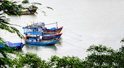 There is a fishing boat on the river. Three boats on the right side are parked. Fishing is a way to make money for the people of Vietnam. View from the shore to the river.