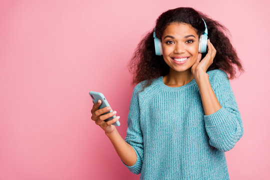 Photo of curly wavy cheerful nice woman wearing headphones modern technology standing near empty space with telephone isolated pastel color background