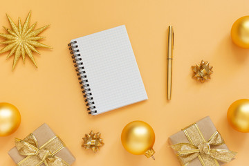 Holiday background, gold background with glitter gold star and gift boxes and christmas balls, open spiral notepad and pen, flat lay, top view, copy space