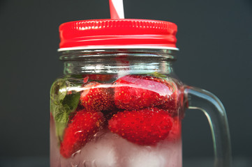 Fresh strawberries close-up while in a cocktail jar. Ripe strawberries in a summer refreshing cocktail on a dark background and copy space.