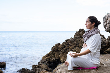 Naklejka na ściany i meble Beautiful pregnant woman is meditating on the beach