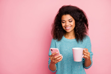 Photo of cheerful toothy beaming cute girl browsing through telephone wearing blue sweater with cup...