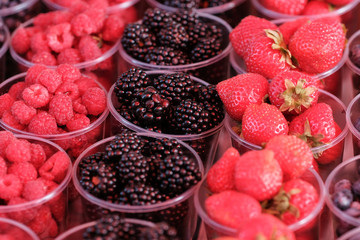 A counter with plastic containers and glasses filled with fresh berries. Blackberry, Strawberry, Blueberry, Raspberry. Food market.