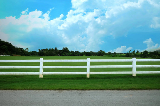 Landscape of farm with split rail fence. White short fence in the field. Landscape farm with cloudy and blue sky.
