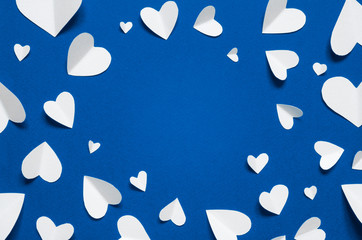 Frame with white paper hearts at blue backdrop, top view. Color of the year 2020 Classic Blue. Copy...