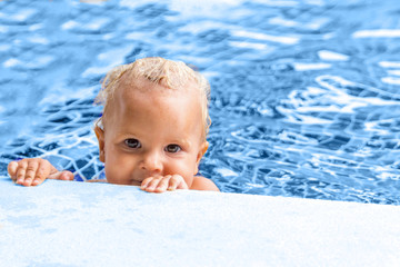Fototapeta na wymiar Cute baby swims in a swimming pool in sunny summer day, toned in classic, blue color, og the year. Childhood and toys concept.