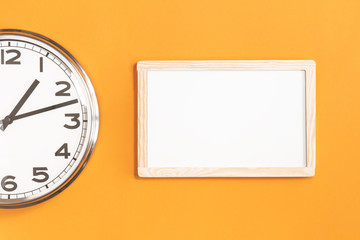 Part of analogue plain wall clock with white board on trendy saffron orange background. One...