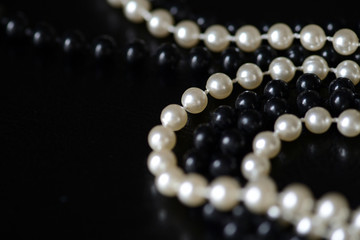 Fragment of a necklace of black and white beads on a black background close-up. Fashion background