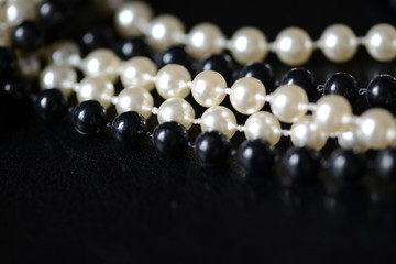 Fragment of a necklace of black and white beads on a black background close-up. Fashion background