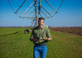Young farmer standing in wheat field and setup irrigation system on tablet. © Zoran Zeremski