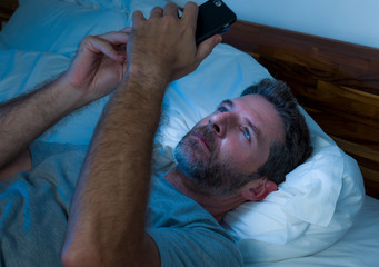 young attractive and relaxed man with blue eyes lying on bed late at night in dark and dim light...
