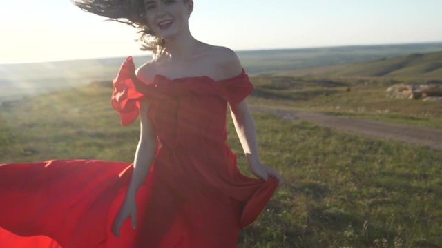 Blurred image of a woman in a red dress running across the field and laughing her hair and clothes evolving in the wind