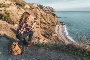 Young hip woman with a backpack exploring and photographing the coast on a beautiful day. Concept of exploration and adventures