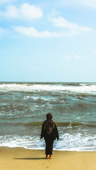 The view from behind of a Malay girl with hijab looking to the ocean taking a walk at tropical beach.