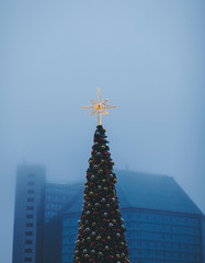 Fototapeta premium decorated with shining Christmas star and baubles on background of the misty city