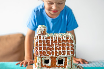 Сute little boy eats gingerbread house and having fun. Kid enjoy Christmas traditions. Child broke...