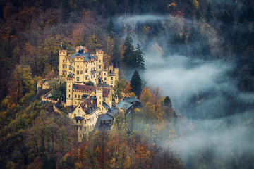 Aerial view of famous Hohenschwangau bavarian castle with a beautiful fog on the forest in autumn season