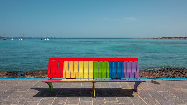 Rainbow bench facing inland in Corralejo, pride colors painted sitting or resting area, symbol of LGBT community or acceptance and inclusiveness concepts, in Fuerteventura, Canary Islands, Spain