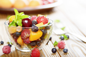 Assorted fruits in glass bowl on kitchen wooden table with fork aside