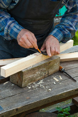 a senior carpenter doing measurements on a piece of wood outdoors during a sunny day