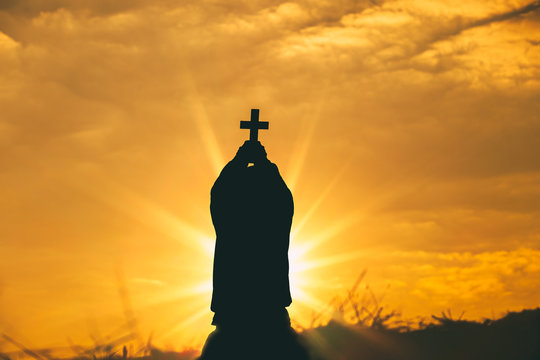 Man kneeling down and Raise the Cross to sky for praying to God at sunset background. christian silhouette concept.