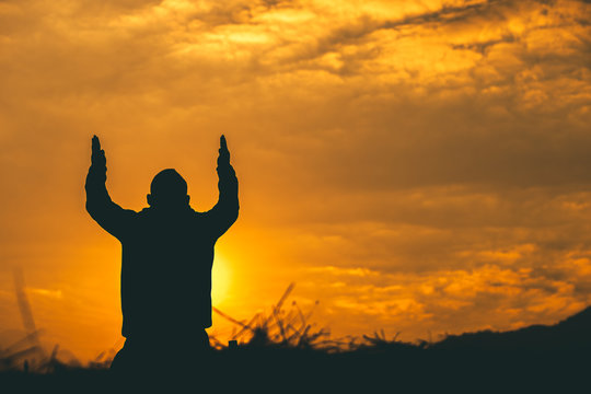 Man kneeling down and raise two hands to sky for praying to God at sunset background. christian silhouette concept.