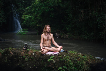 Fototapeta premium Yoga practice and meditation in nature. Man practicing near river
